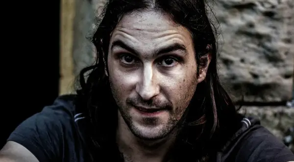 Primer plano de un hombre con cabello largo y oscuro, mirada intensa y piel con un efecto dragan photoshop que acentúa las texturas.