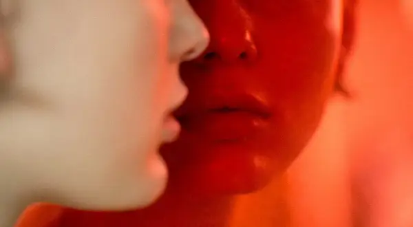 Primer plano de dos rostros, uno iluminado en rojo intenso, el otro en tonos claros. Martina Matencio captura un momento íntimo y enigmático.