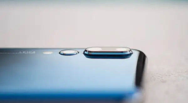 Detalle de la cámara de un smartphone azul, mostrando el módulo de lentes Leica y la tecnología de pixel binning para capturar más luz.