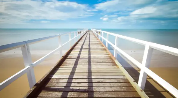 Un muelle de madera se extiende hacia el mar azul bajo un cielo nublado. La foto perspectiva crea una sensación de profundidad y calma.