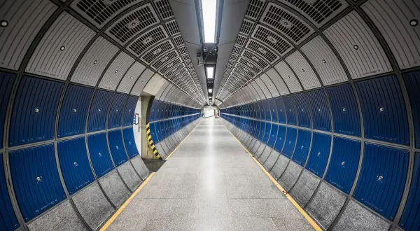 Pasillo circular de metro con paneles azules y grises, y líneas convergentes que crean una perspectiva infinita.