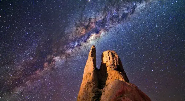 Rocas imponentes bajo la vía láctea en el cielo nocturno.