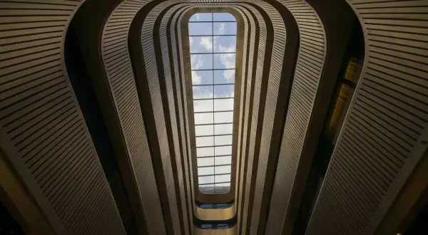 Interior de un edificio con un tragaluz rectangular. Las paredes curvas y las barandillas crean un efecto de túnel, jugando con formas geométricas básicas.