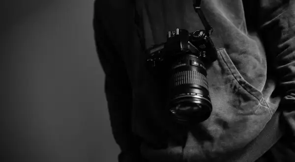 Cámara colgada del cuello de un sudadera, lista para capturar momentos como los de los fotógrafos famosos actuales.