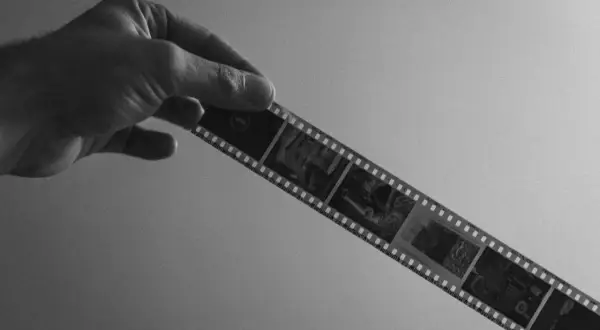 Mano sostiene tira de película en blanco y negro, lista para rebelar foto. Se aprecian imágenes de coches antiguos.