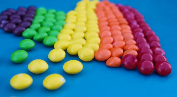 Caramelos de colores forman un arcoíris, demostrando la ley de contraste con sus vibrantes tonos sobre el fondo azul.