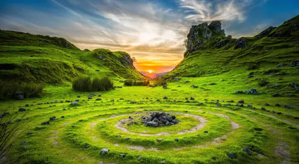 Paisaje verde con un círculo de piedras y un atardecer vibrante, capturado con técnica qué es HDR para resaltar detalles.