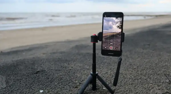Un tripode casero sostiene un teléfono móvil en la playa, listo para grabar el mar y el cielo.