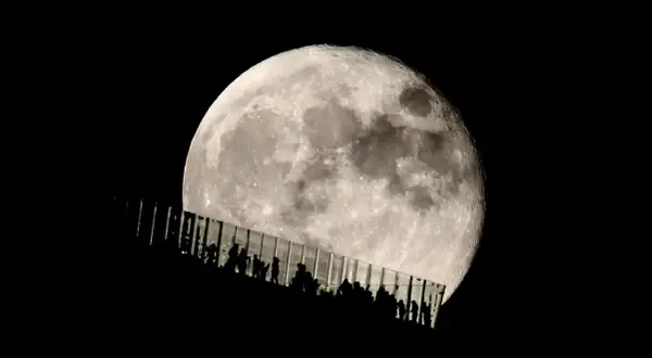 Siluetas de personas observan la luna llena desde una pasarela de cristal. Los parámetros de la foto de la luna capturan su textura y brillo.