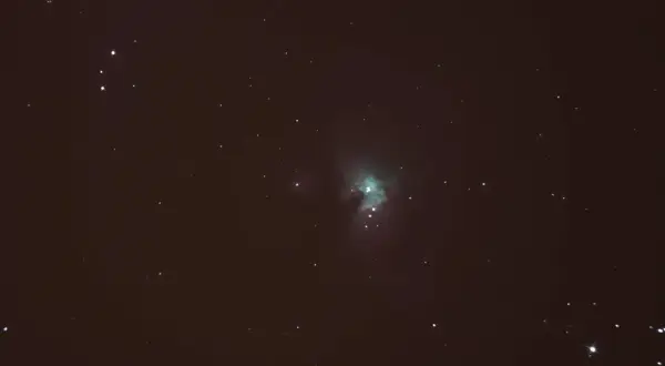 Nebulosa verdosa en el cielo nocturno, rodeada de estrellas y con tenues estelas de estrellas.