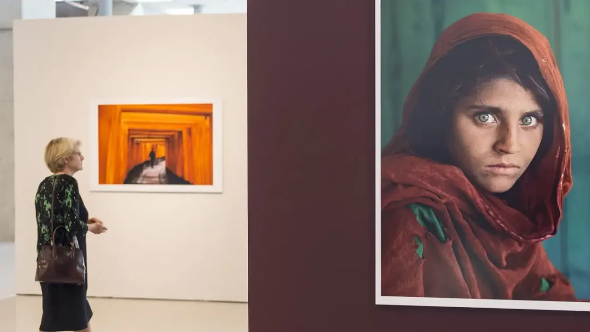 Una mujer observa una obra de Steve McCurry, destacando la icónica mirada de la niña afgana.