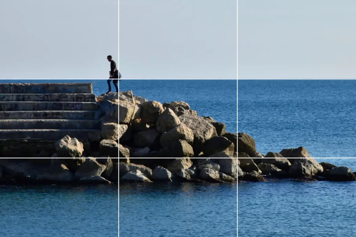 Un hombre camina por unas escaleras de piedra hacia el mar, siguiendo la regla de los tercios vertical.