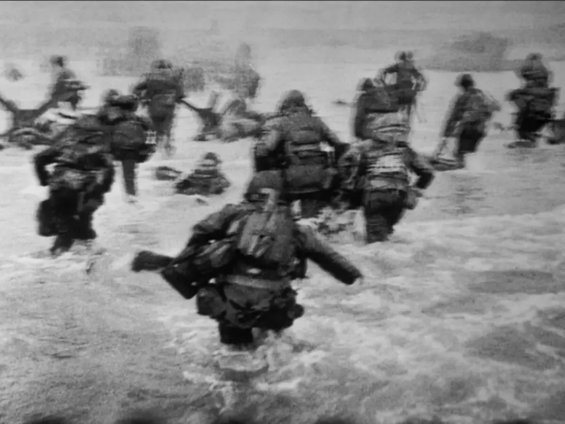 Soldados avanzan en el agua durante el desembarco de Normandía, una escena icónica capturada por Robert Capa.