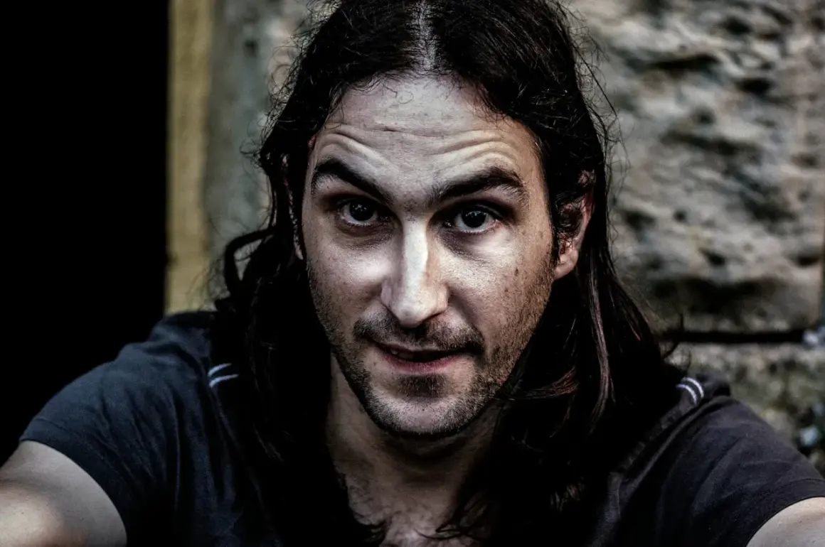 Primer plano de un hombre con cabello largo y oscuro, mirada intensa y piel con un efecto dragan photoshop que acentúa las texturas.