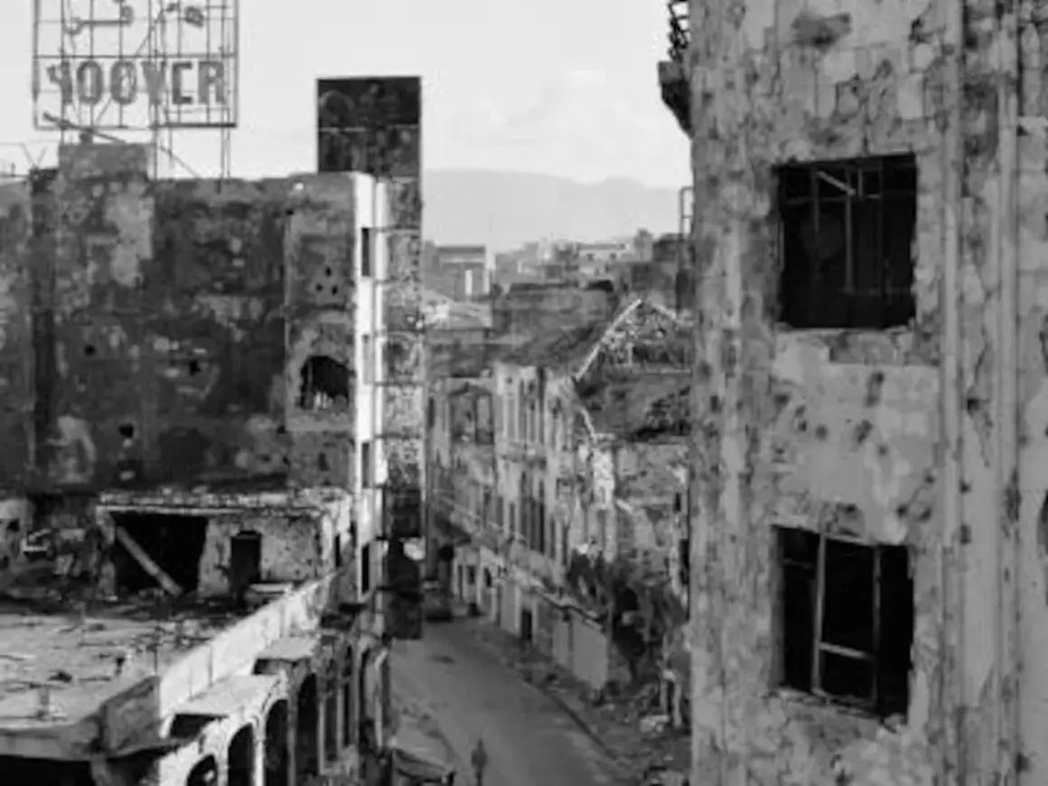 Calle devastada con edificios en ruinas, un cartel de "HOOVER" en lo alto. La mirada de Gabriele Basilico captura la desolación.