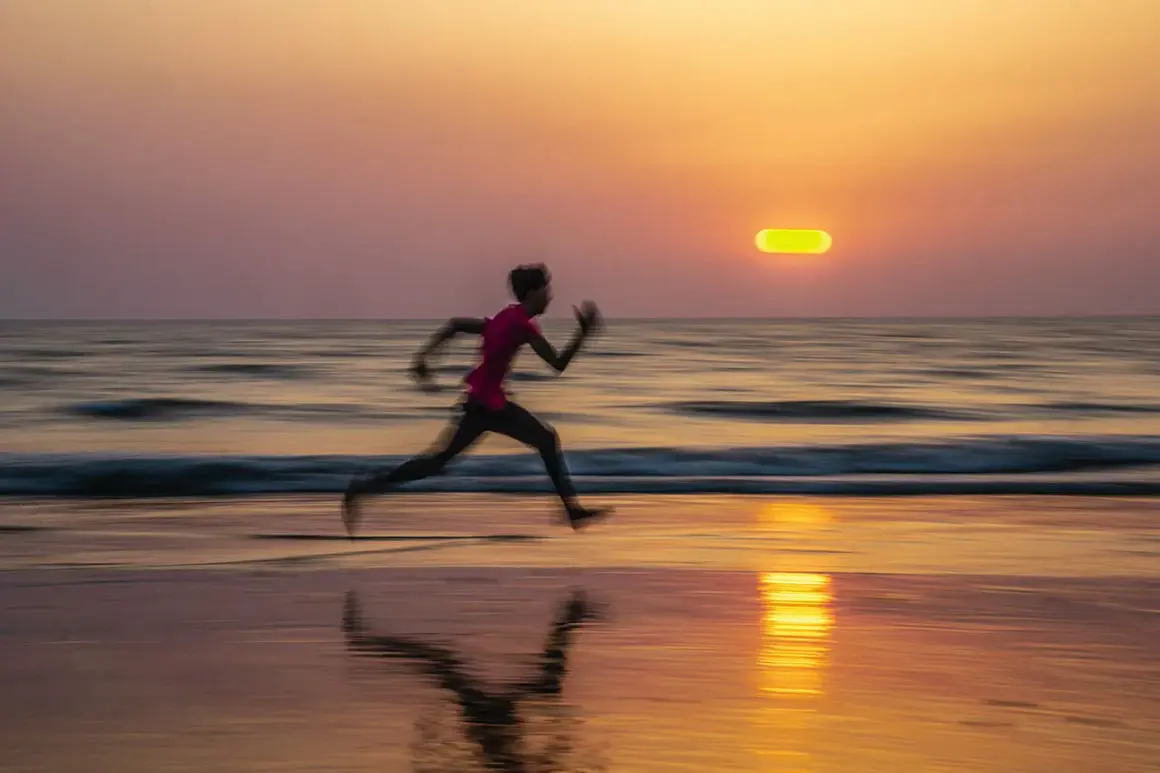 Un corredor se mueve velozmente en la playa al atardecer. El barrido fotográfico captura el movimiento y los colores cálidos del cielo y el mar.
