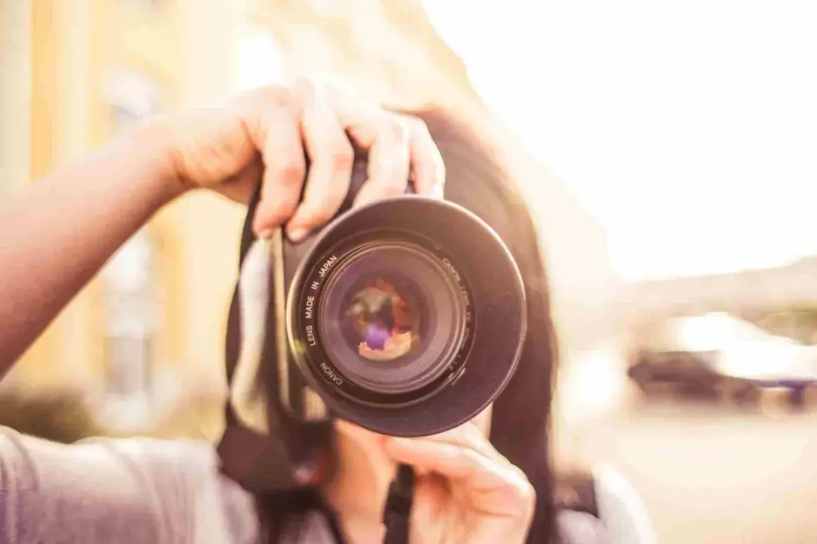 Manos sostienen una cámara Canon, capturando un momento para su proyecto fotográfico. El sol brilla intensamente.