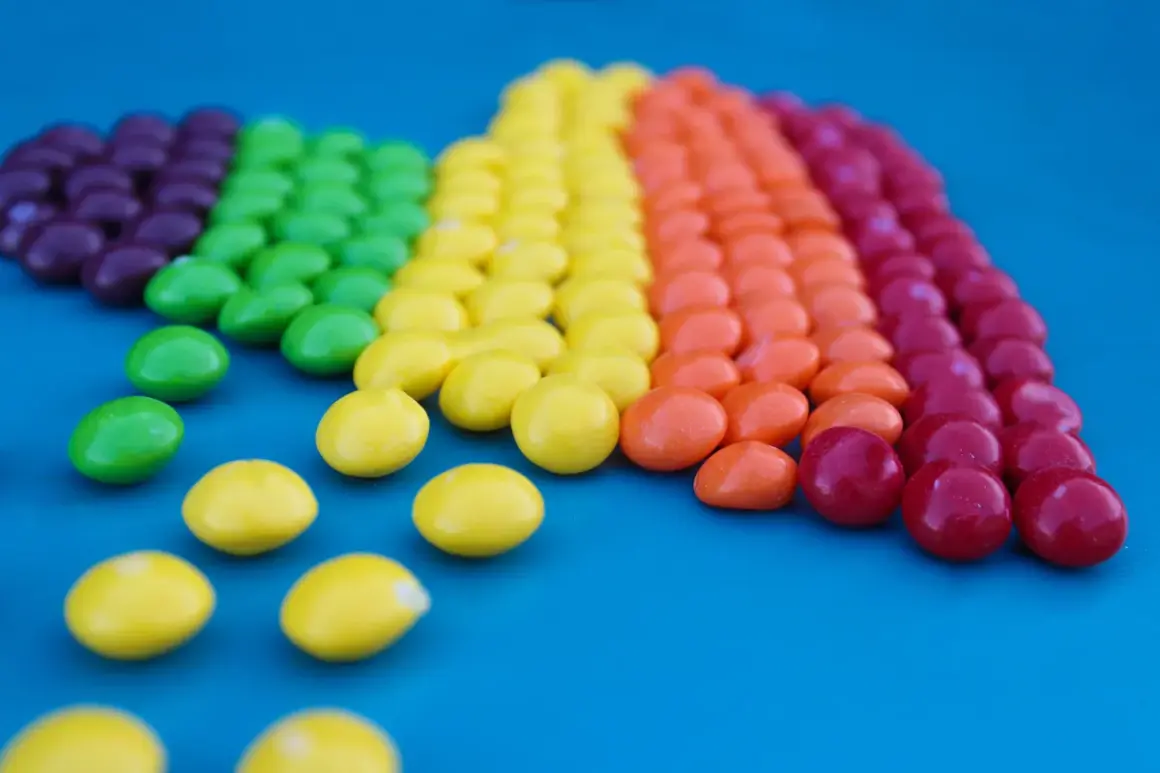 Caramelos de colores forman un arcoíris, demostrando la ley de contraste con sus vibrantes tonos sobre el fondo azul.