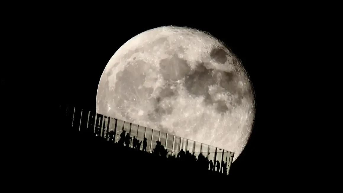 Siluetas de personas observan la luna llena desde una pasarela de cristal. Los parámetros de la foto de la luna capturan su textura y brillo.