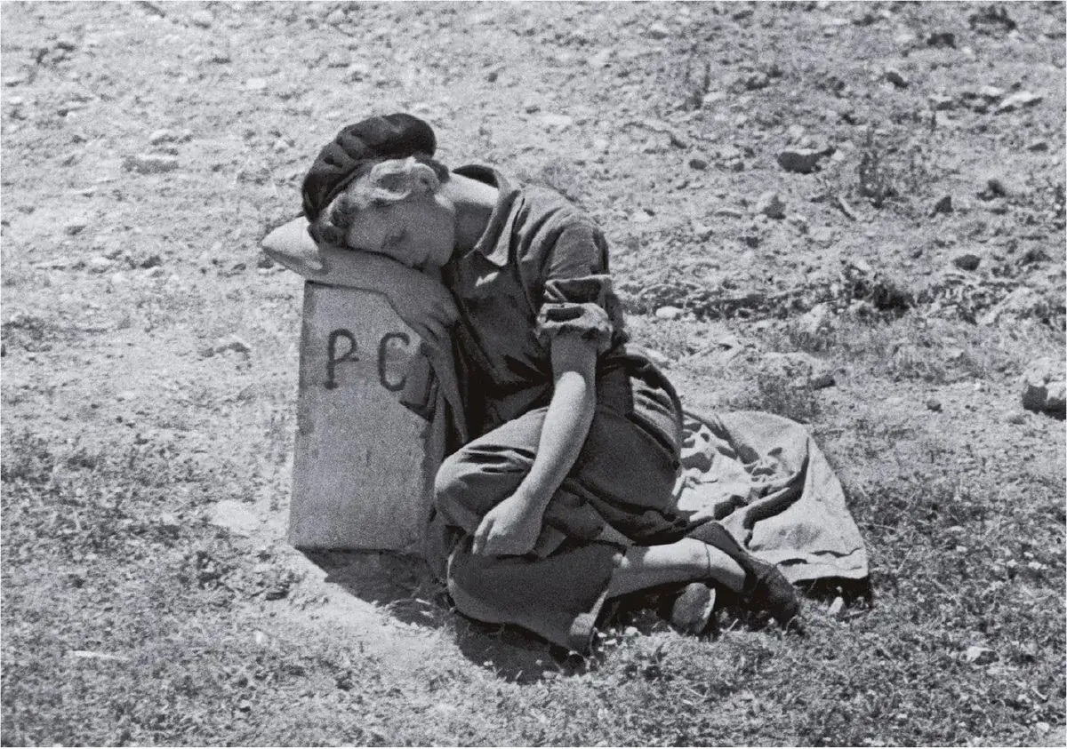 Mujer con boina, vestida de uniforme, duerme apoyada en un poste con 