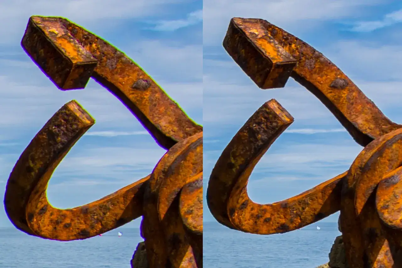 Ancla oxidada con aberraci&oacute;n crom&aacute;tica en el borde verde y morado, contra un cielo azul y el mar.