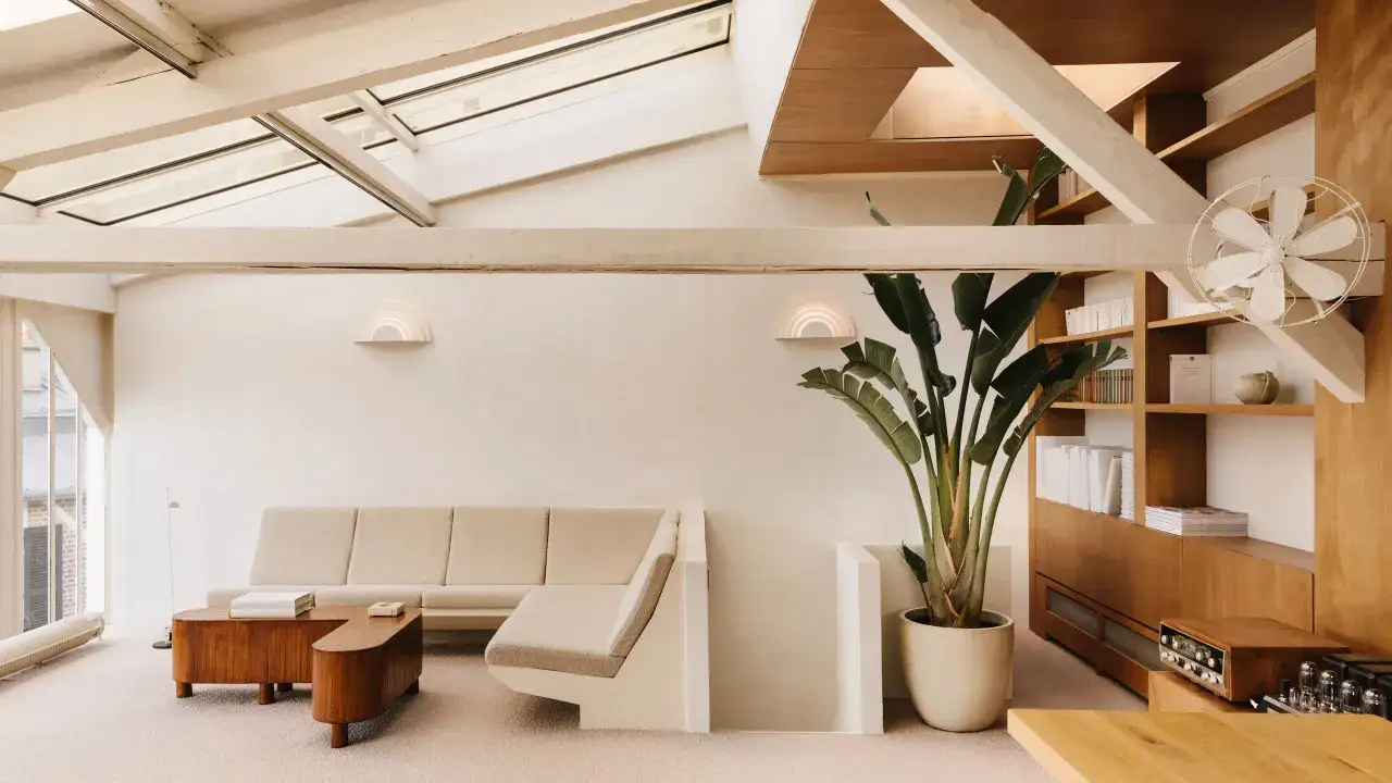 Sof&aacute; modular beige, mesa de centro de madera, planta grande y estanter&iacute;as en una sala de estar con luz natural. Fotograf&iacute;a minimalista.