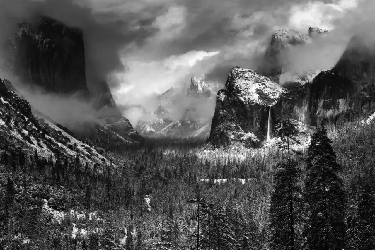 Majestuosas montañas nevadas y un bosque denso, capturados en icónicas ansel adams fotos. Una cascada cae en medio de la niebla.