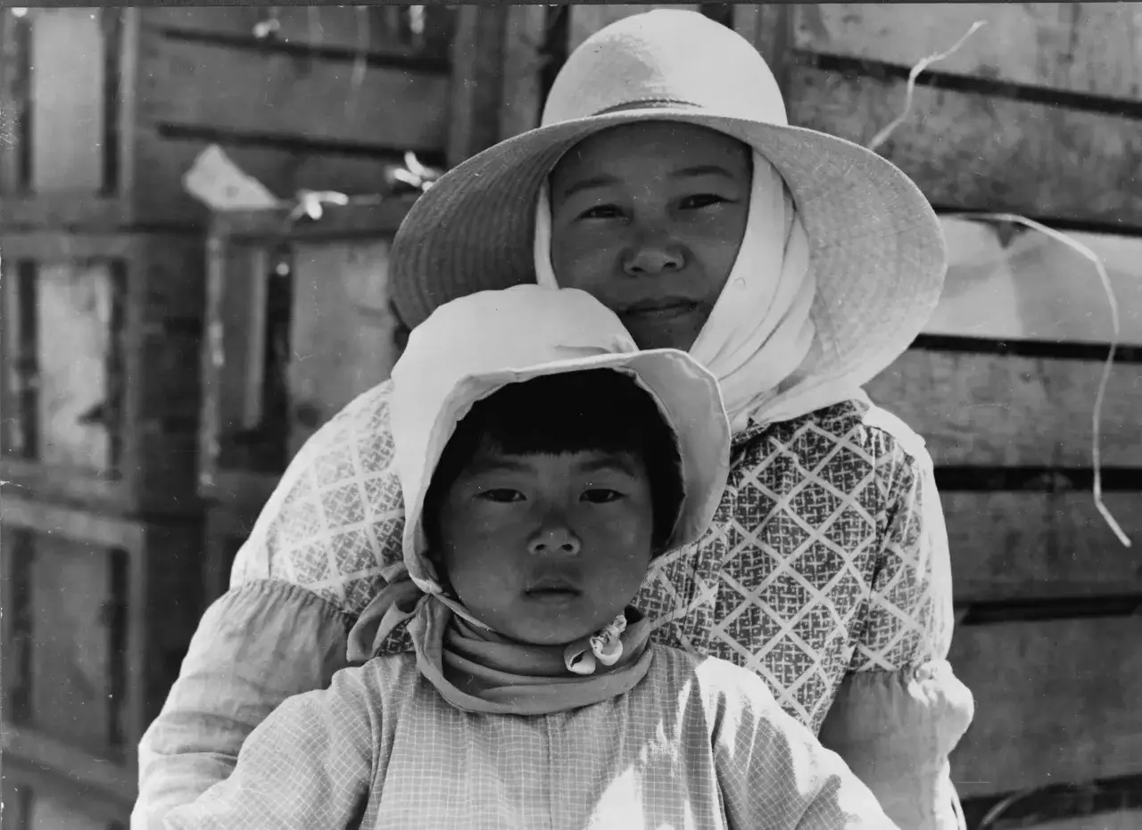 Madre e hijo con sombreros, capturados por Dorothea Lange. El ni&ntilde;o mira fijamente, la madre sonr&iacute;e levemente.