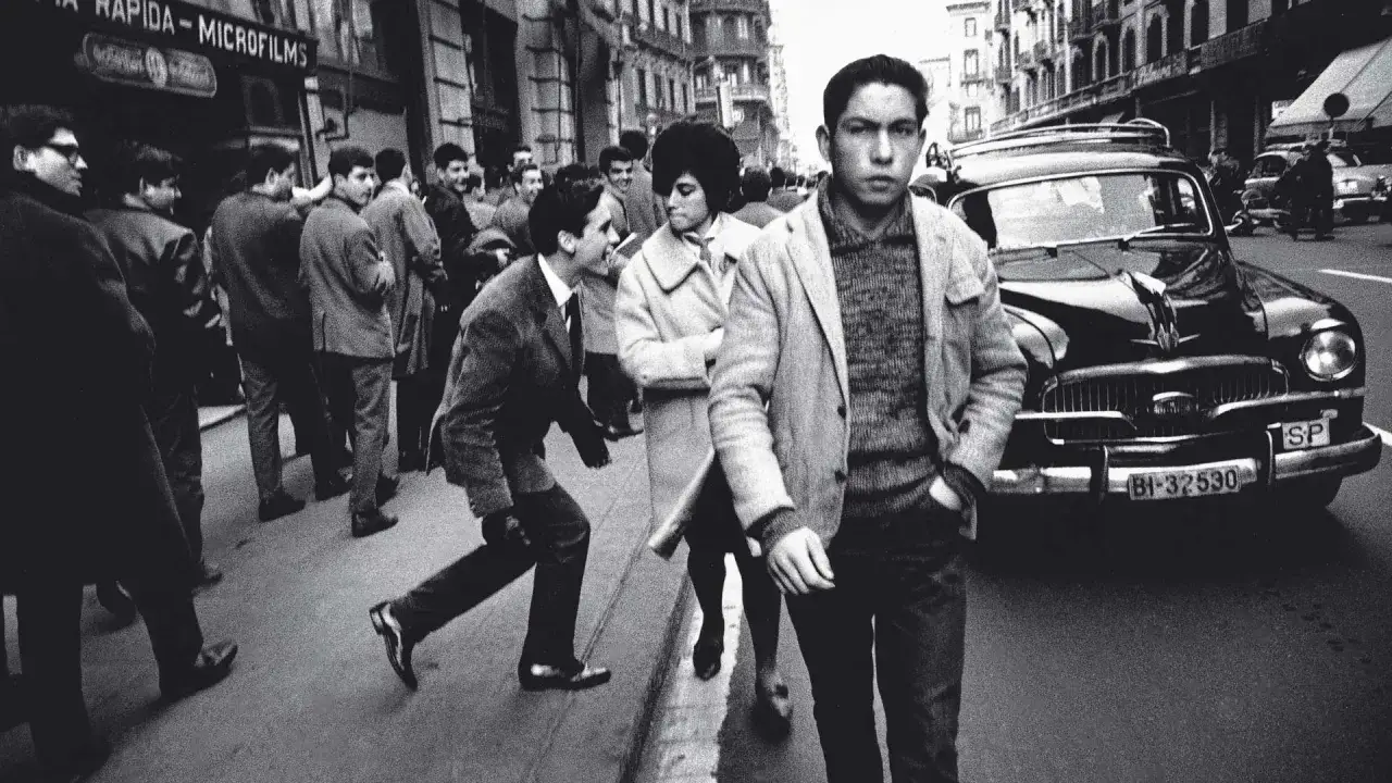 J&oacute;venes viajeros fot&oacute;grafos capturan la vida urbana en blanco y negro, con un coche cl&aacute;sico y gente en la calle.