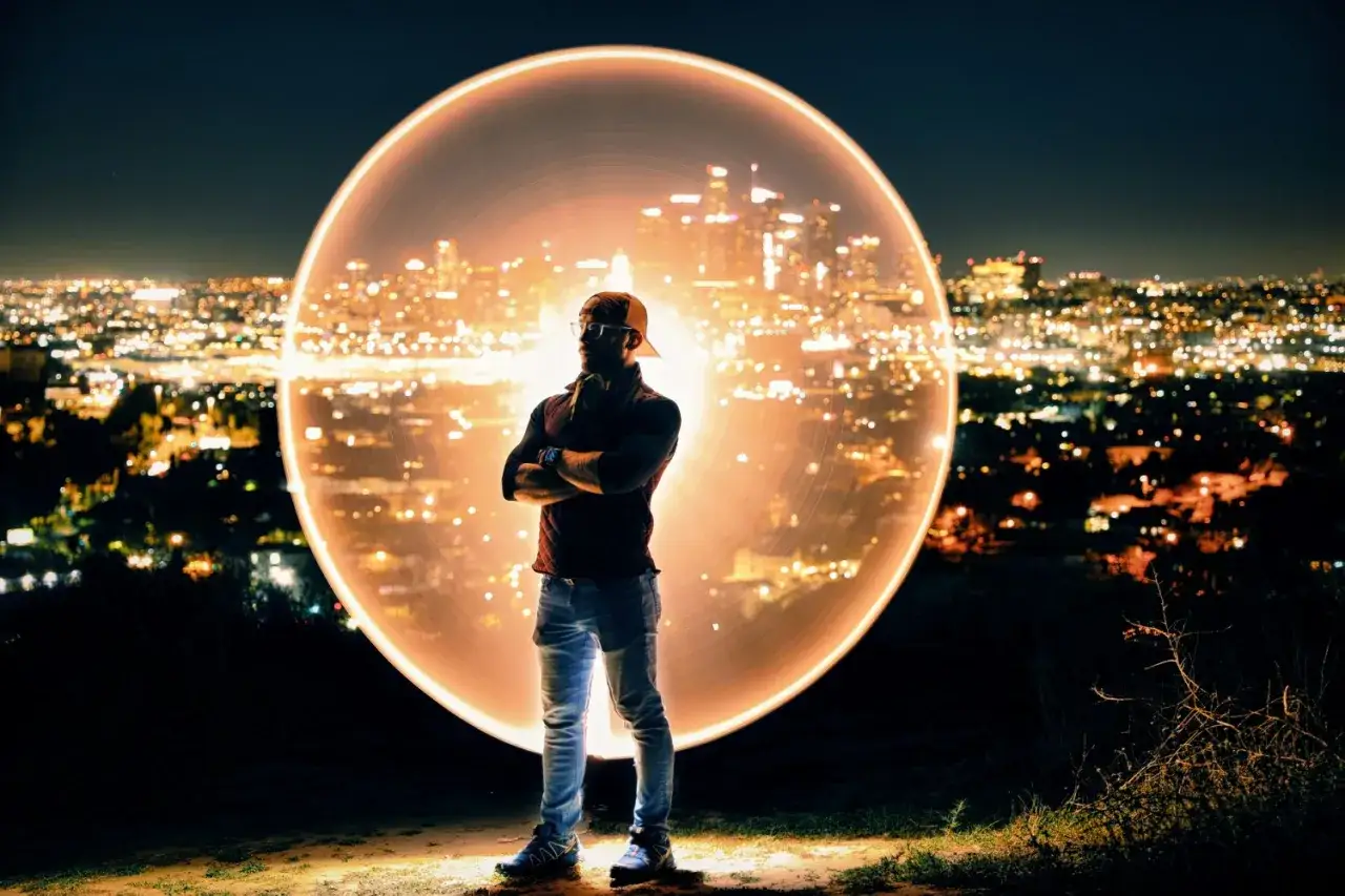 Un hombre con brazos cruzados, en el inicio fotograf&iacute;a de una ciudad iluminada por la noche, envuelto en un halo de luz circular.