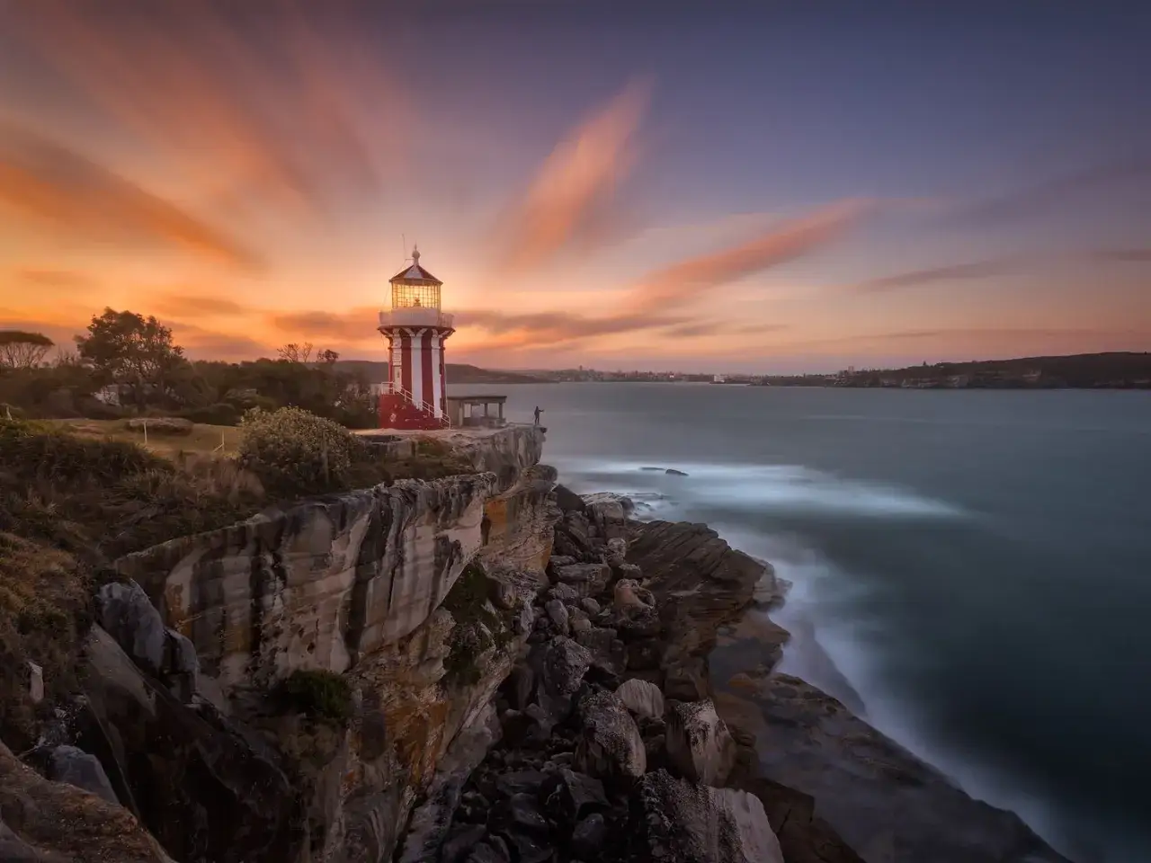 Faro a rayas rojas y blancas en un acantilado rocoso, con el mar y el cielo crepuscular en estas fotos larga exposicion.