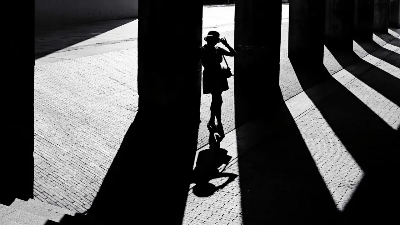Silueta de mujer con sombrero, jugando con las l&iacute;neas impl&iacute;citas de las sombras y la luz sobre el suelo adoquinado.