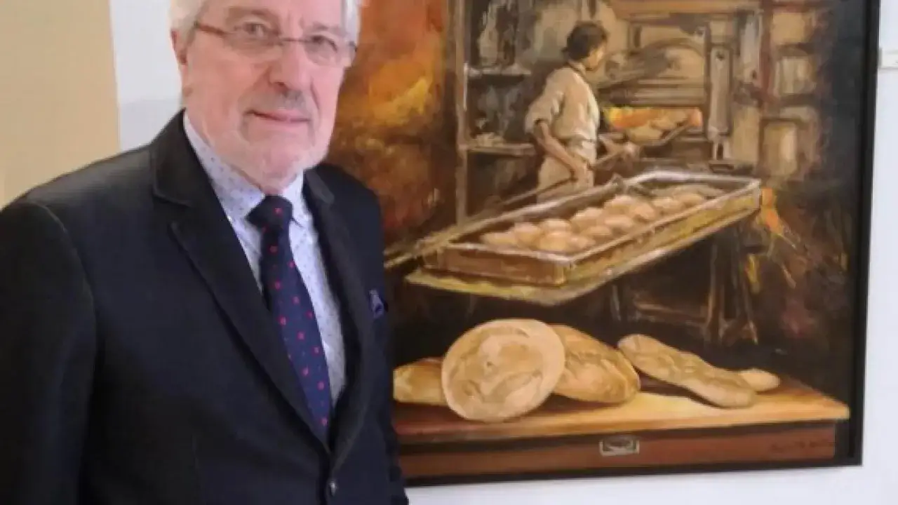 Miguel Soria posa junto a un cuadro que representa una panader&iacute;a antigua, con panes reci&eacute;n horneados y un panadero en acci&oacute;n.