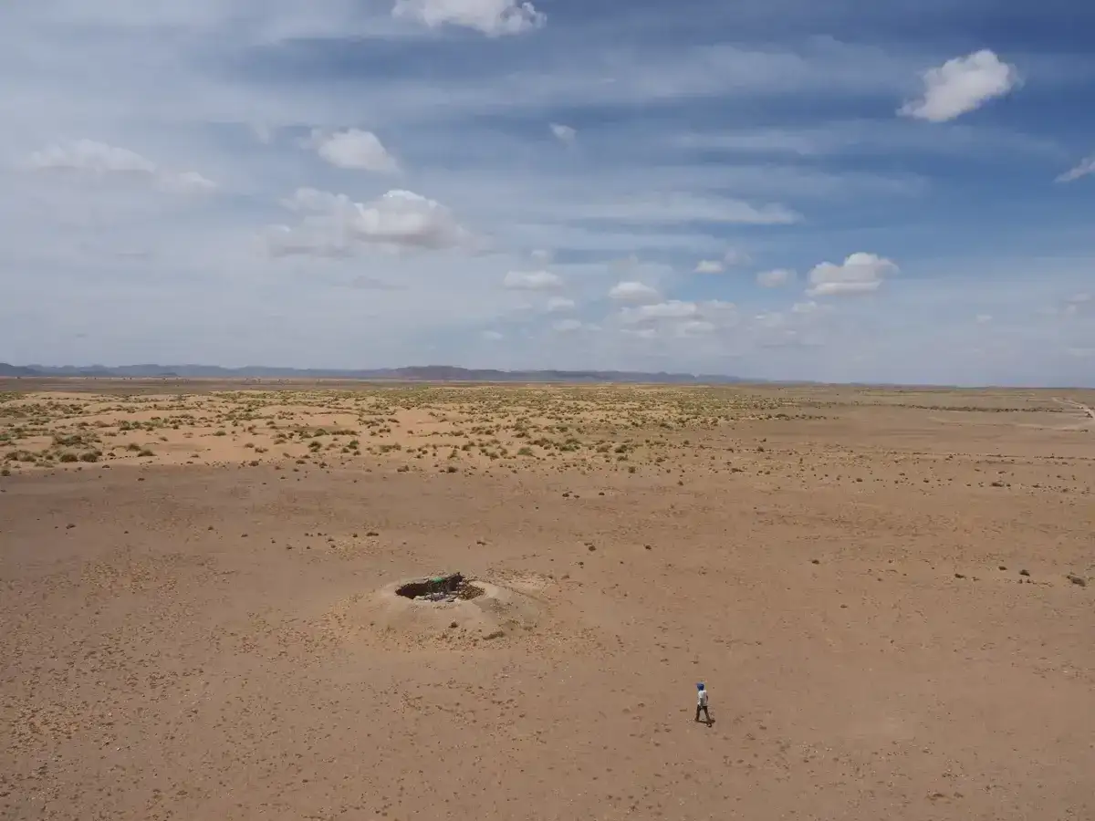 Un hombre camina por un desierto árido, con un cráter lleno de basura en plano nadir.