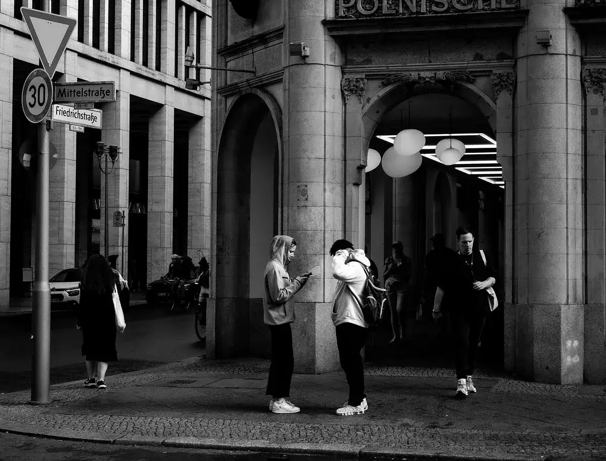 Gente camina bajo arcos, buscando frases sobre luz. Un letrero indica Mittelstraße y Friedrichstraße.