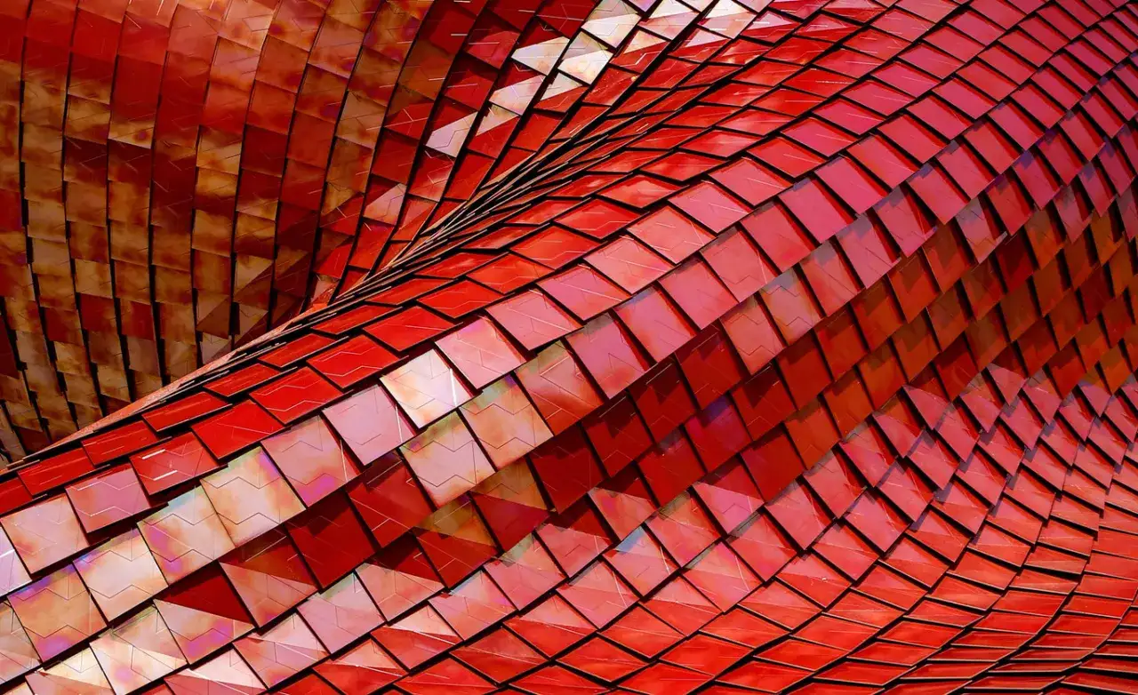 Detalle de la fachada de un edificio con escamas rojas iridiscentes, como si fueran las de un dragón. Fotos originales que capturan la textura y el brillo.