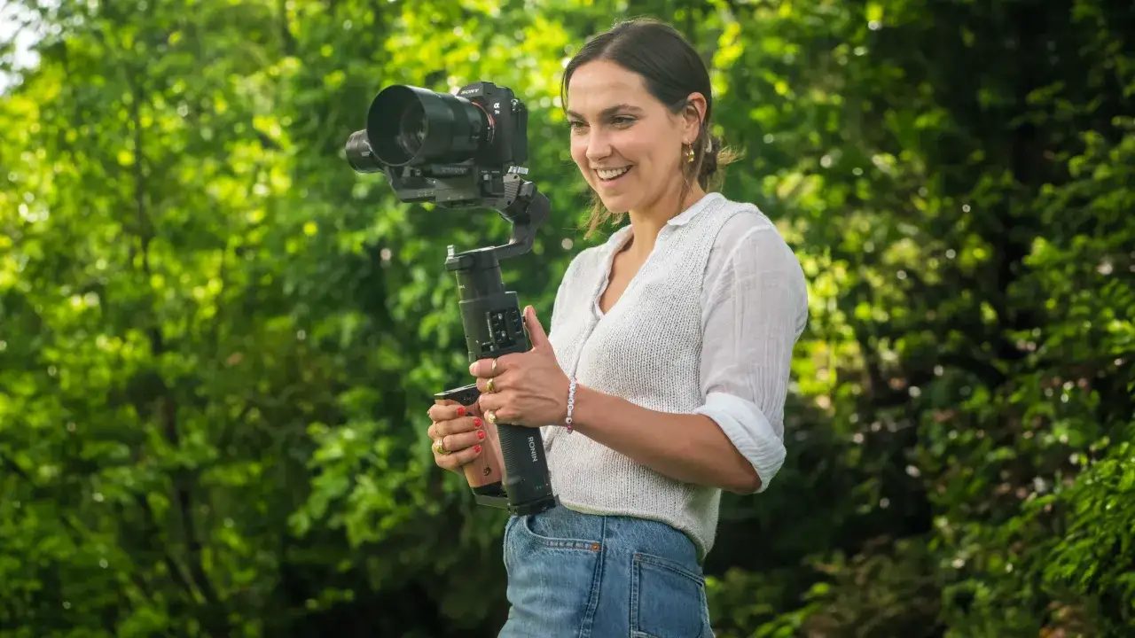 Mujer sonriente sostiene una c&aacute;mara profesional montada en un gimbal, un estabilizador que permite tomas fluidas.