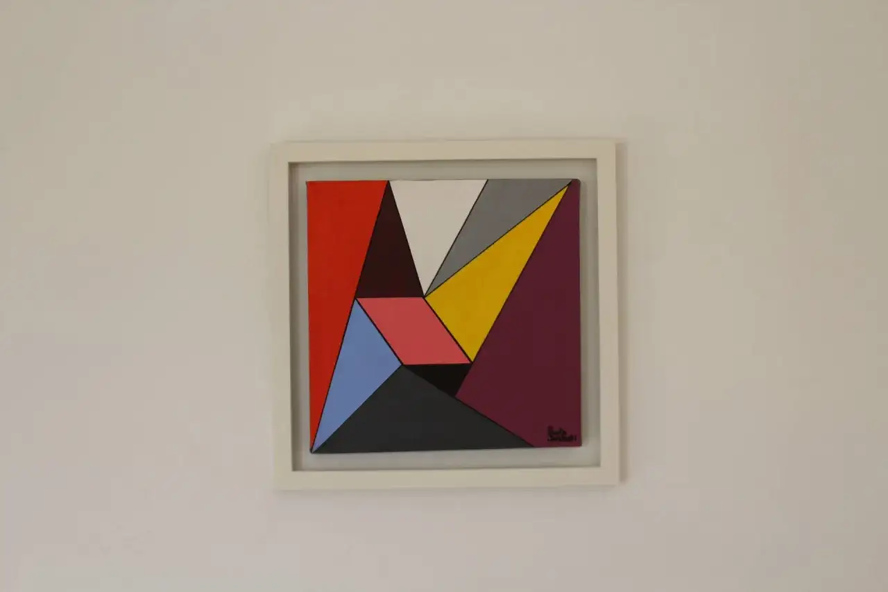 Cuadro con forma abstracta, compuesto por polígonos de colores vibrantes como rojo, amarillo, azul y morado, sobre un fondo blanco.