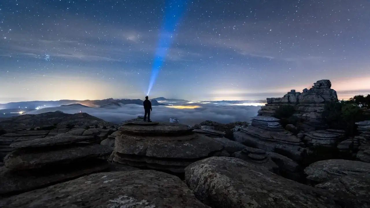 Persona con linterna ilumina el cielo estrellado sobre un mar de nubes. Un paisaje perfecto para fotos Perseidas.
