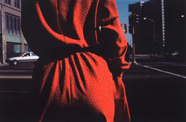 Un vestido rojo con pequeños triángulos blancos, capturado por harry callahan photography, se funde con las sombras de una calle urbana.