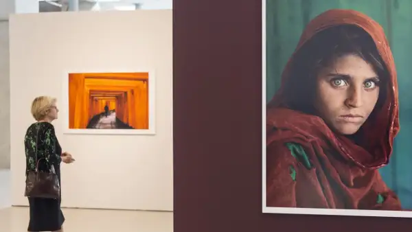 Una mujer observa una obra de Steve McCurry, destacando la icónica mirada de la niña afgana.