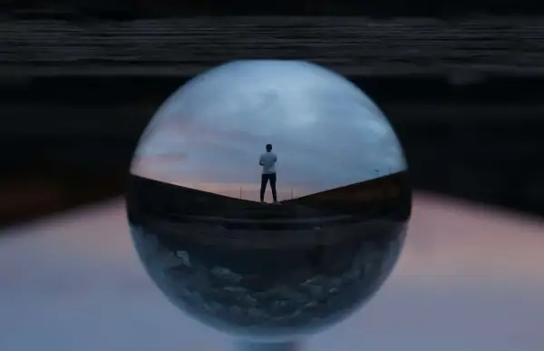 Un hombre mira el atardecer a través de una esfera de cristal, creando fotos originales y creativas.