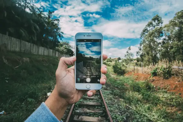 Mano sujeta móvil para capturar vía de tren. ¡Descubre trucos para hacer fotos originales y únicas!