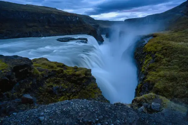 Cascada imponente con agua que cae en un cañón, creando un **efecto seda** bajo un cielo nublado.
