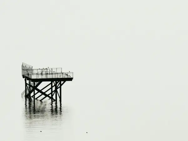 Plataforma solitaria sobre el agua, reflejo nítido. Fotografía minimalista que evoca calma y soledad.