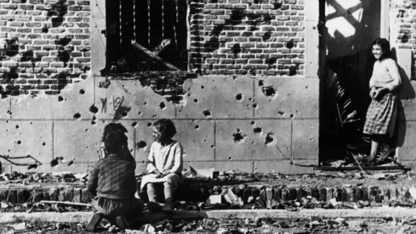 Niños juegan entre escombros frente a un edificio bombardeado, una escena conmovedora capturada en una de las robert capa fotos famosas.