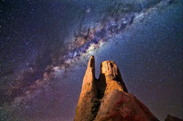 Rocas imponentes bajo la vía láctea en el cielo nocturno.