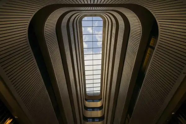 Interior de un edificio con un tragaluz rectangular. Las paredes curvas y las barandillas crean un efecto de túnel, jugando con formas geométricas básicas.