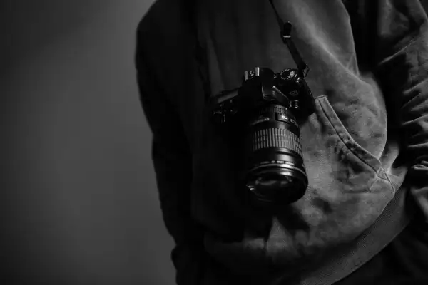 Cámara colgada del cuello de un sudadera, lista para capturar momentos como los de los fotógrafos famosos actuales.