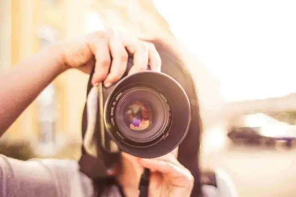 Manos sostienen una cámara Canon, capturando un momento para su proyecto fotográfico. El sol brilla intensamente.